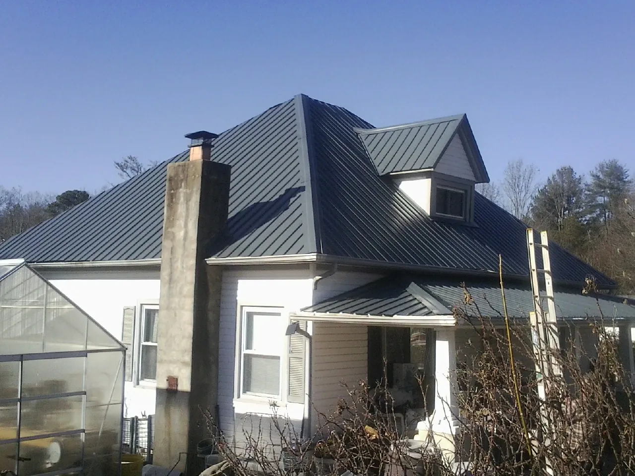 Dark blue standing seam metal roof on a white farmhouse with dormer — Slate & Tile Roof Repair by Roofing Brothers in Rancho Cucamonga