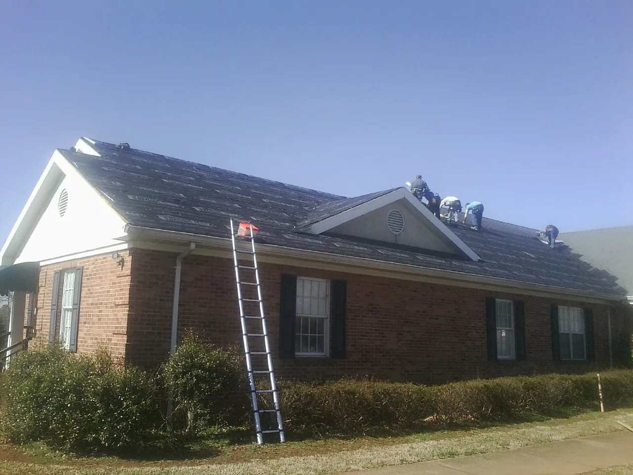 Crew tearing shingles off a brick ranch roof with a ladder set — Emergency Roof Repair work by our crew in Rancho Cucamonga