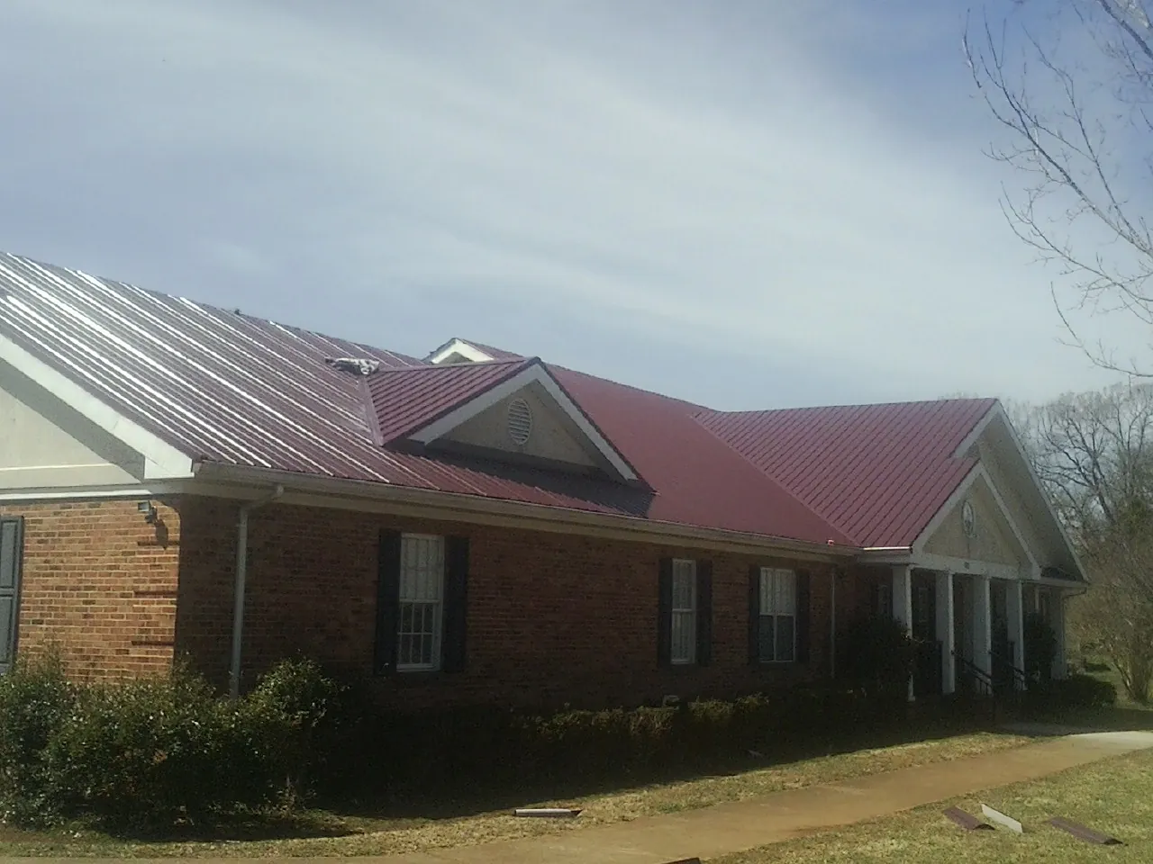 Red metal roof with gabled entries on a long brick building, from a Hail Damage Roof Repair job in Rancho Cucamonga
