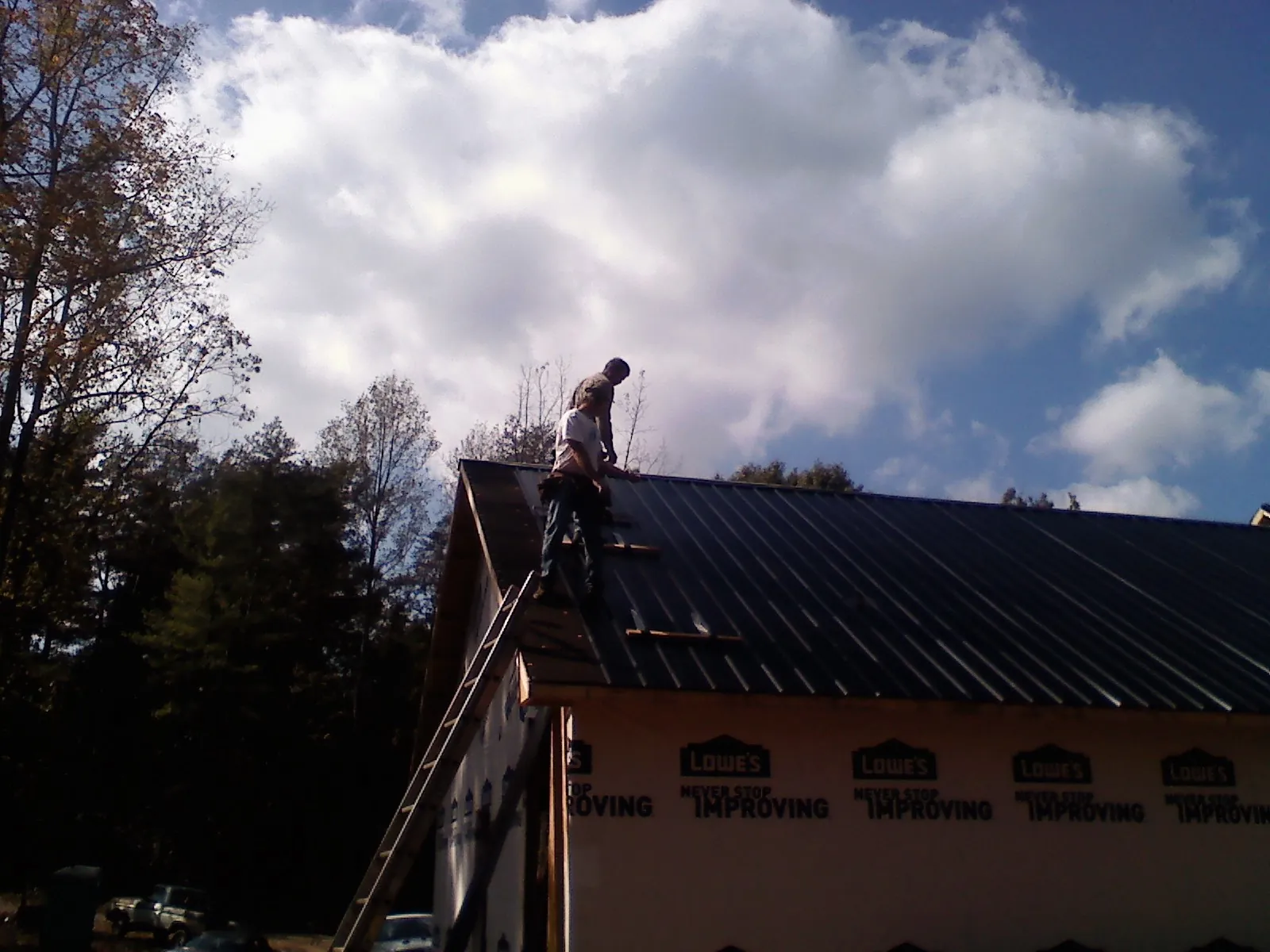 Roofer fastening dark metal panels high against a cloudy sky, from a Roof Inspection job in Rancho Cucamonga